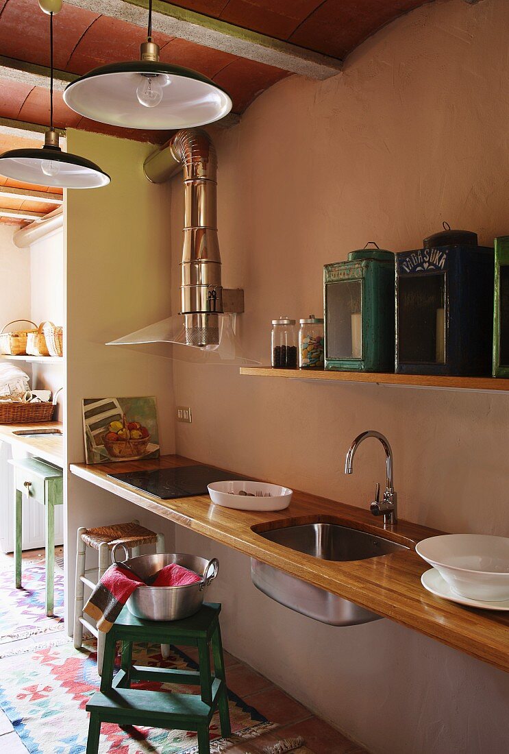 Simple, floating kitchen counter with wooden worksurface and sink mounted in niche below vintage lanterns on floating shelf in retro-style, open-plan interior