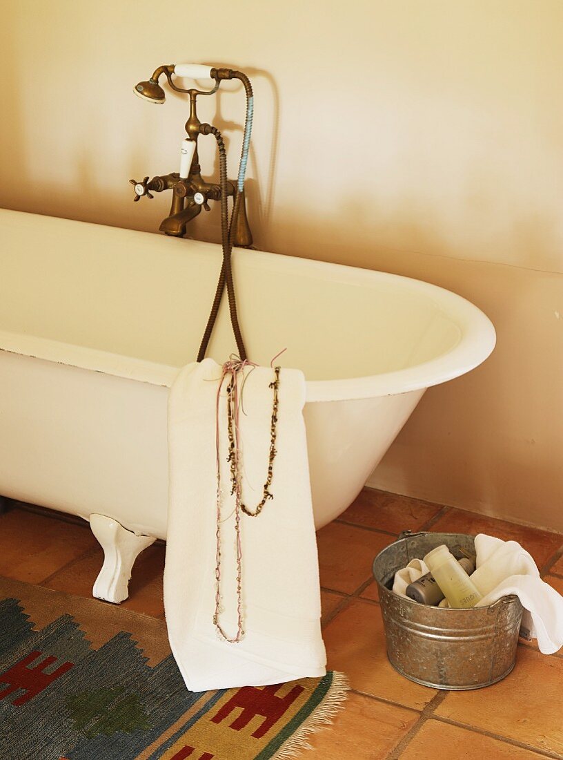 Toiletries on terracotta floor next to vintage, claw foot bathtub with brass tap fittings