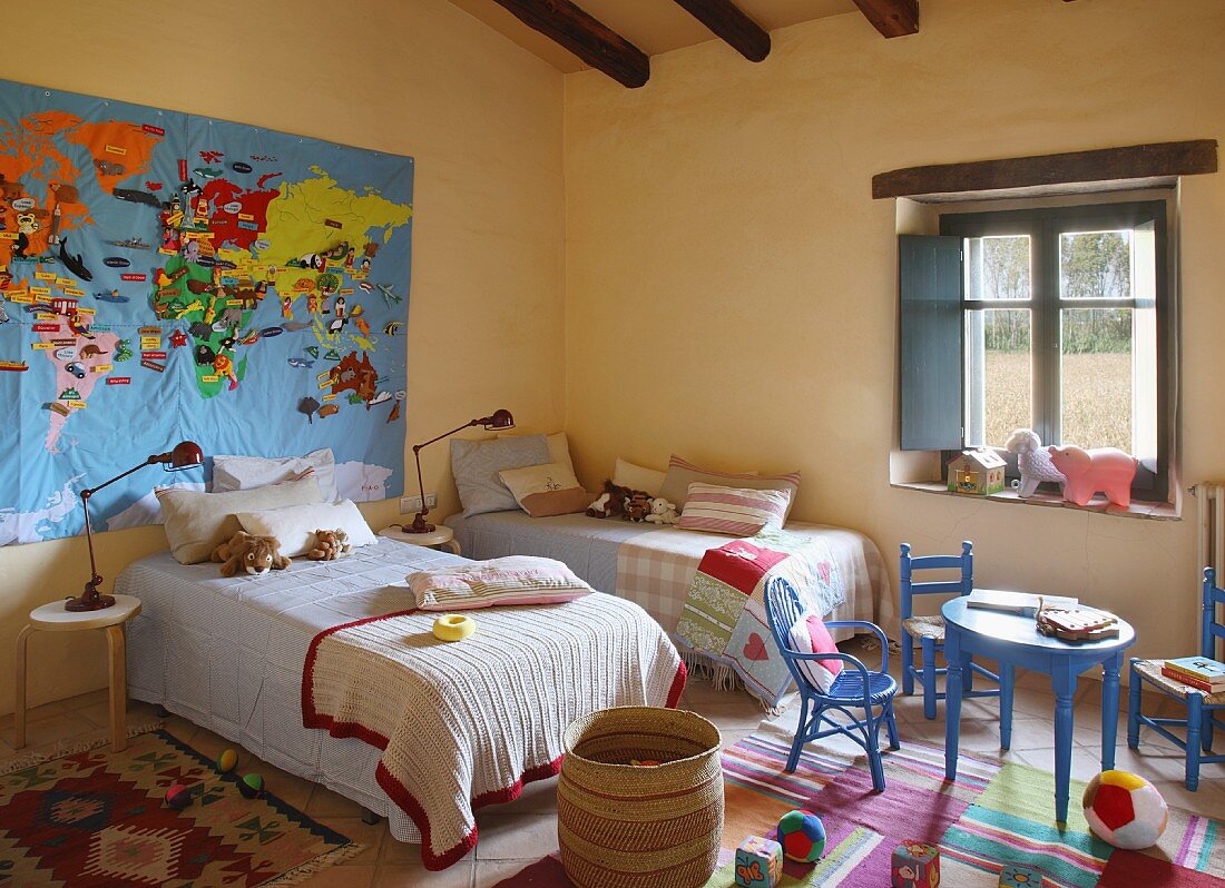 Gelbgetöntes Schlafzimmer mit Einzelbetten und blaue Kinderstühle um Tisch vor dem Fenster