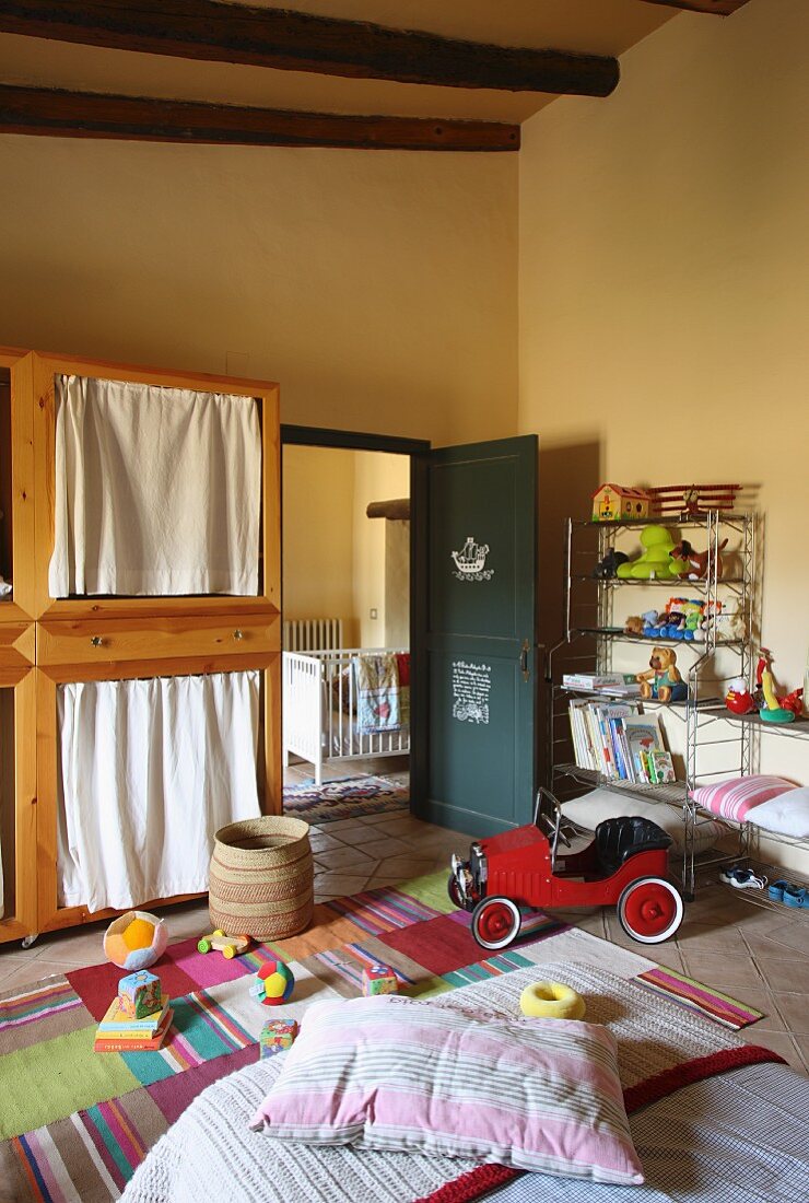 Gelb getöntes Schlafzimmer mit Spielzeugen und Kinderfahrzeug vor offener Tür