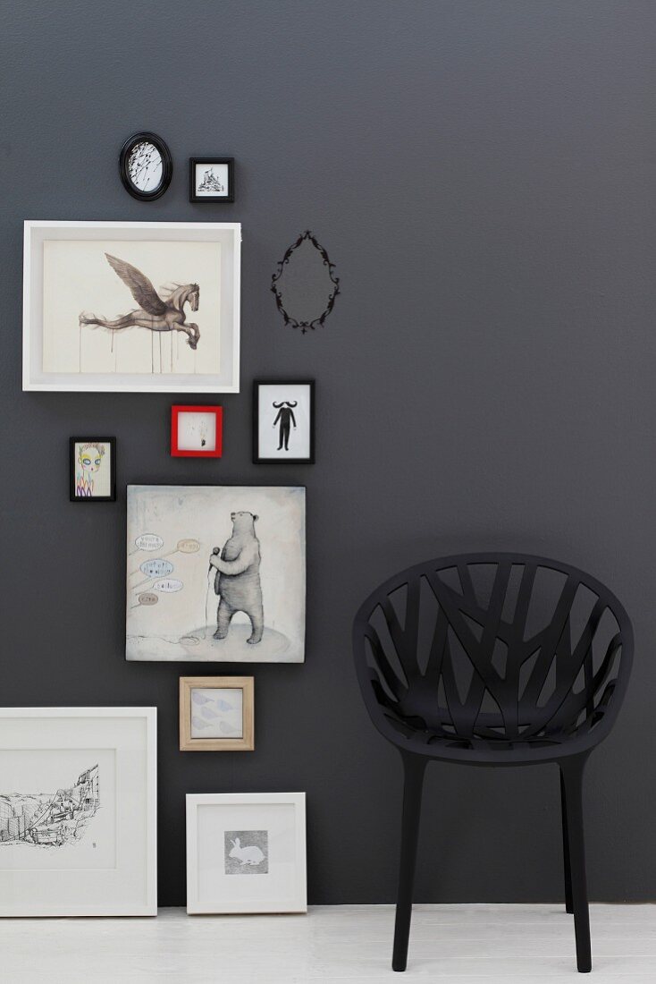 Schwarze, geflechtartiger Kunststoffstuhl vor schwarzer Wand mit Bildern und Tiermotiven