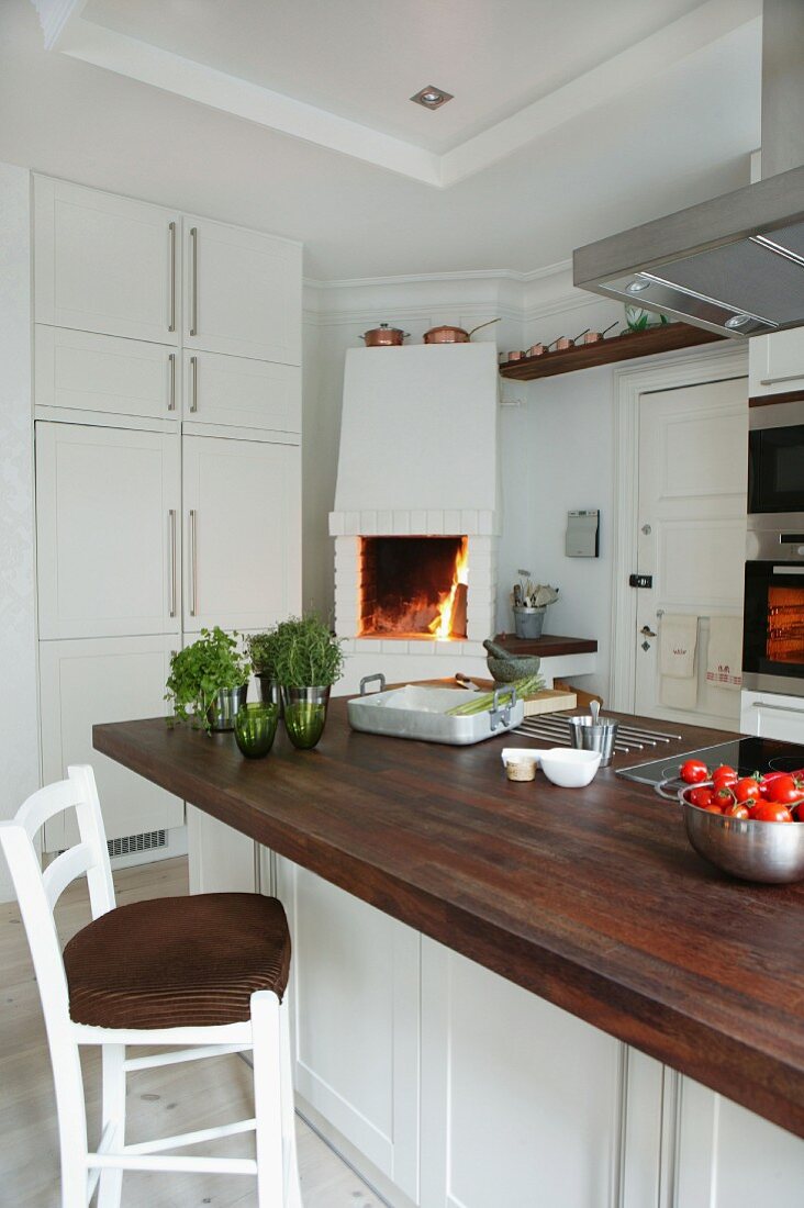 Mittelblock mit Holz- Arbeitsplatte und Barhocker in in weisser Küche mit offenem Kamin