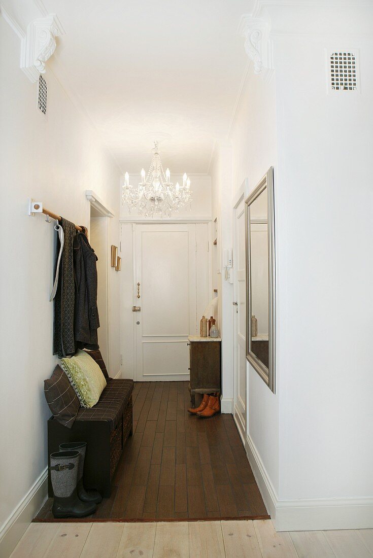 Coat rack in narrow hall with traditional chandelier hanging from ceiling