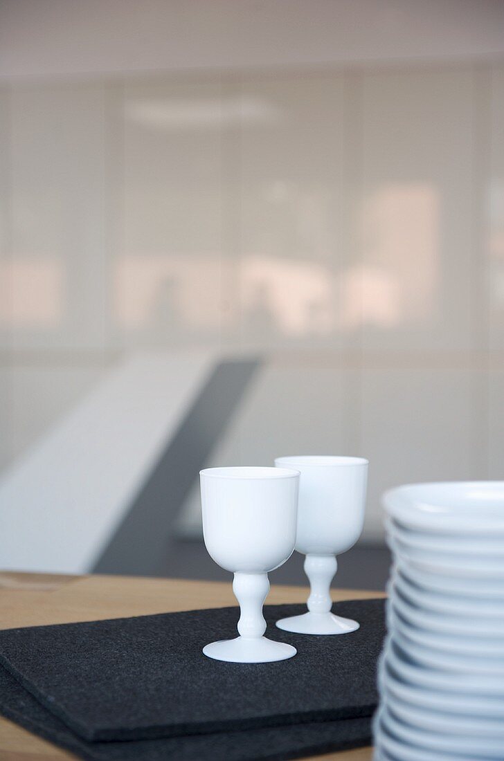 Porzellanbecher auf schwarzer Filzmatte neben Tellerstapel auf Tisch