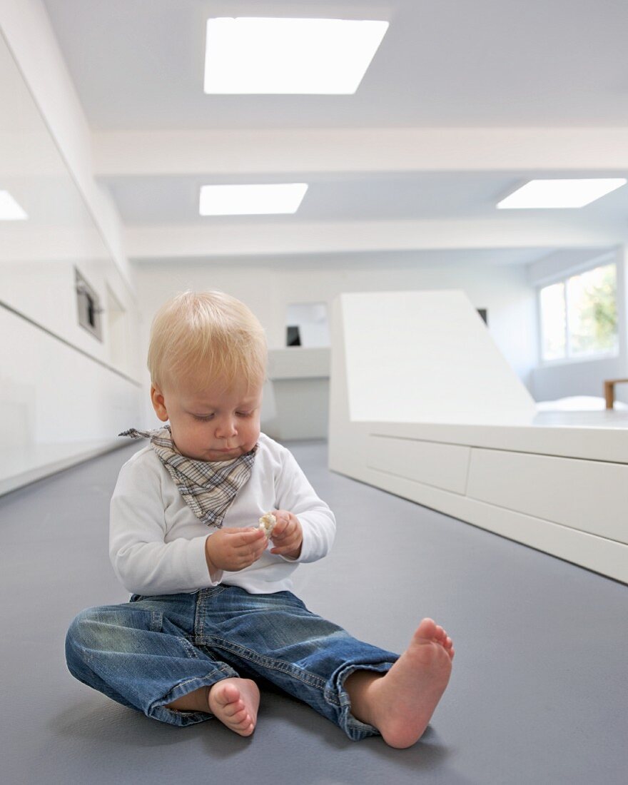 Kleines Kind sitzt auf Boden neben weisser, futuristischer Sitzbank in zeitgenössischem Wohnraum