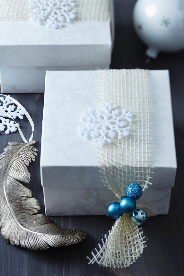 Verpacktes Weihnachtsgeschenk mit stilisierter Schneeflocke und türkisfarbenen Minikugeln an einem Netzband