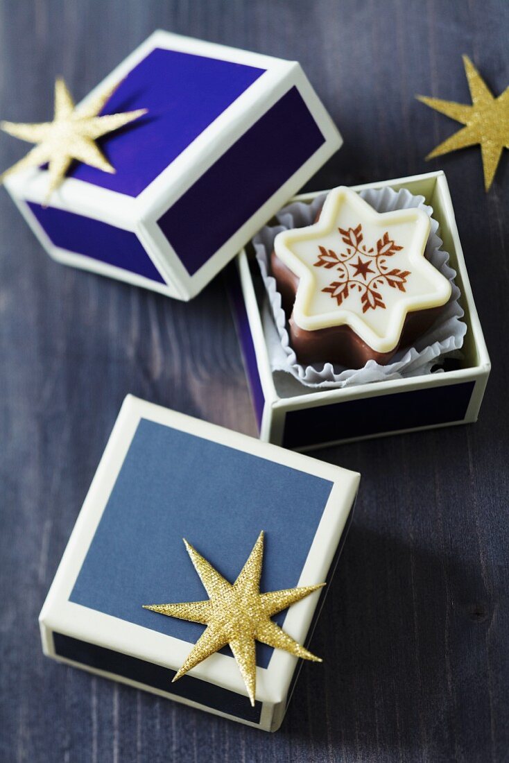 Sternförmige Weihnachtspralinen in kleinen blauen Schachteln mit goldenem Glitzerstern