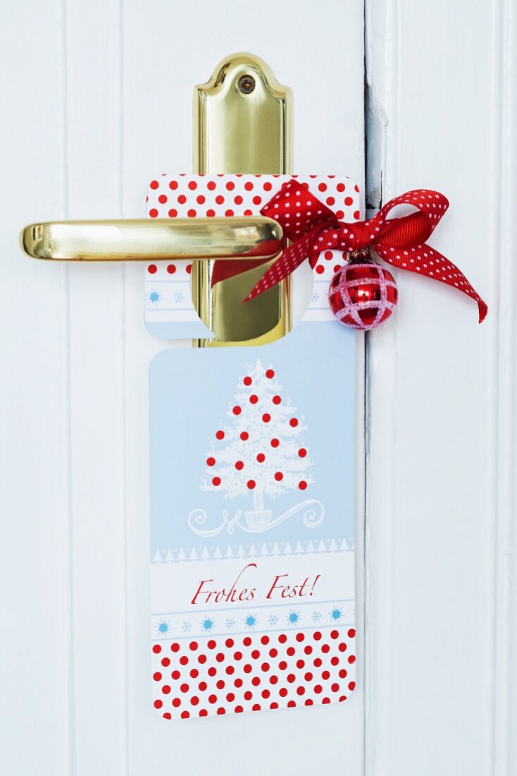 Weihnachtlischer Türschild mit roter Baumkugel und Schleife an Messingtürgriff
