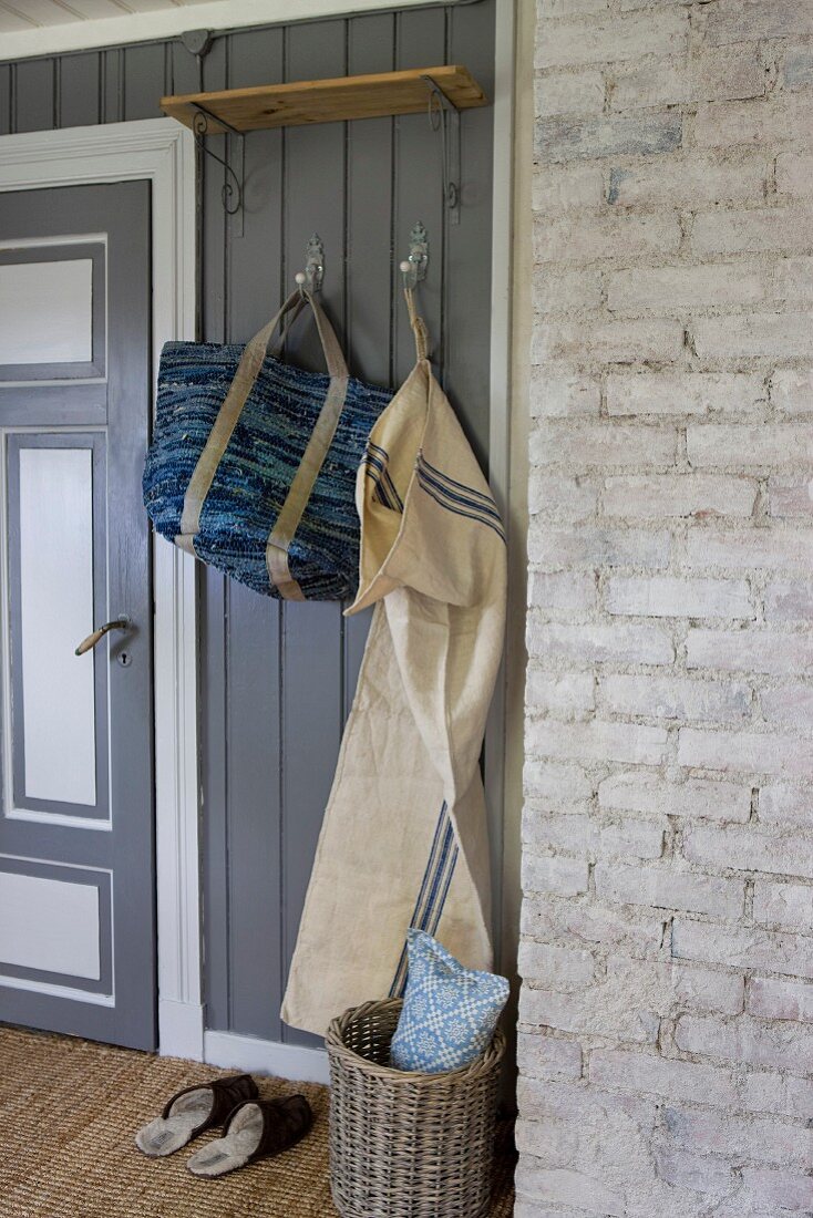 Aufgehängte Tasche und Wäschesack an Garderobenhaken im Hausflur mit grauer Holzverkleidung