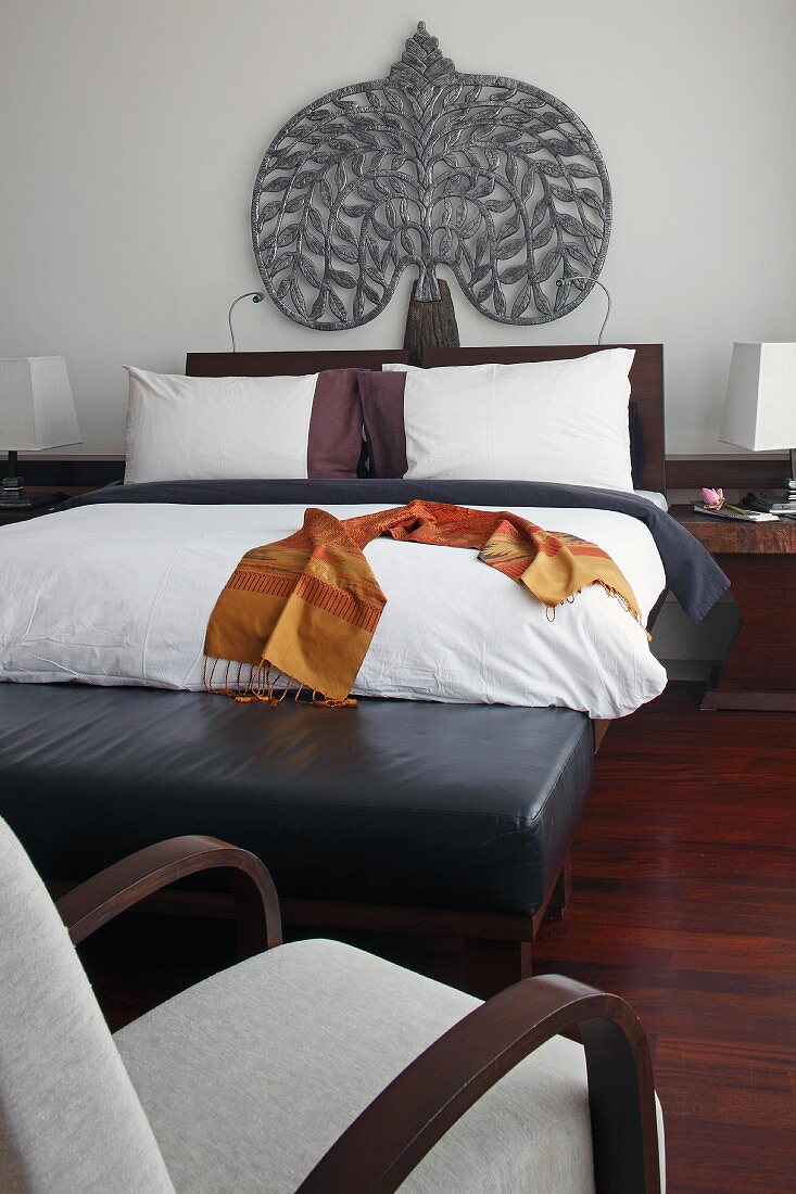 Doppelbett mit folkloristischer Kopfteilverzierung und schwarzlederne Kleiderbank im Hotelzimmer