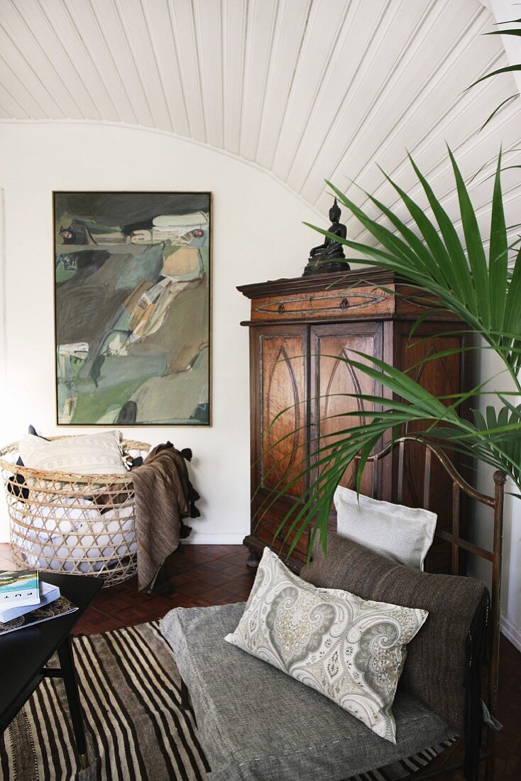 Wohnzimmerecke mit antikem Schrank und Malerei; Metallstuhl mit Kissen auf Webteppich