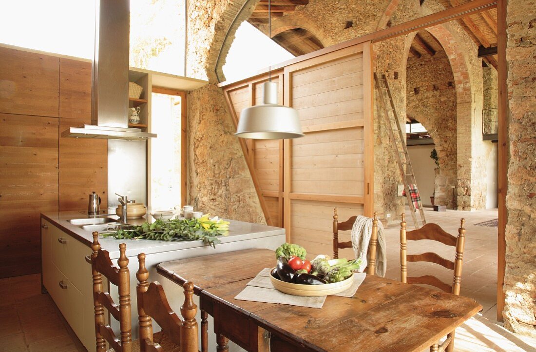 Modern kitchen island and dining area with turned, Spanish wooden chairs in spacious, restored stone house