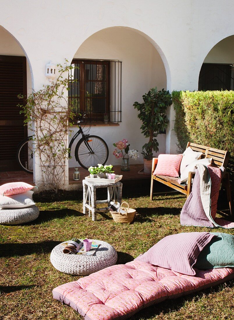Sonnenbad im Vorgarten mit Polsterlandschaft auf dem Rasen vor mediterranem Wohnhaus mit Arkaden