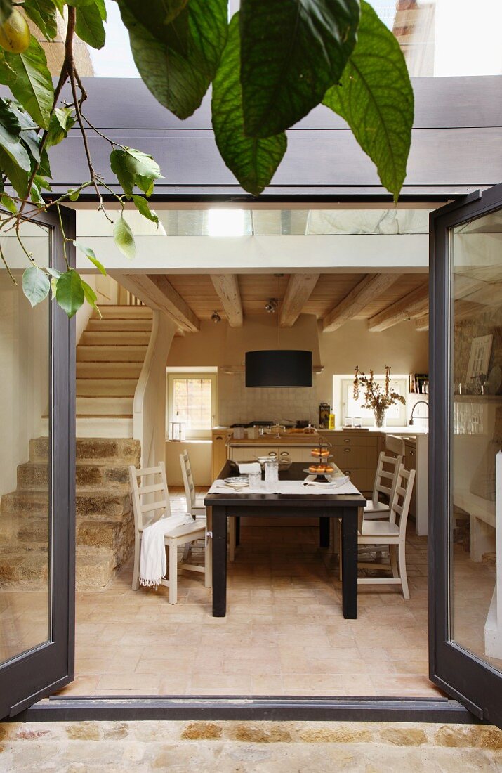 Blick durch offene Terrassentür eines modernen Wohnhauses auf Essplatz vor Küche neben gemauerter Treppe