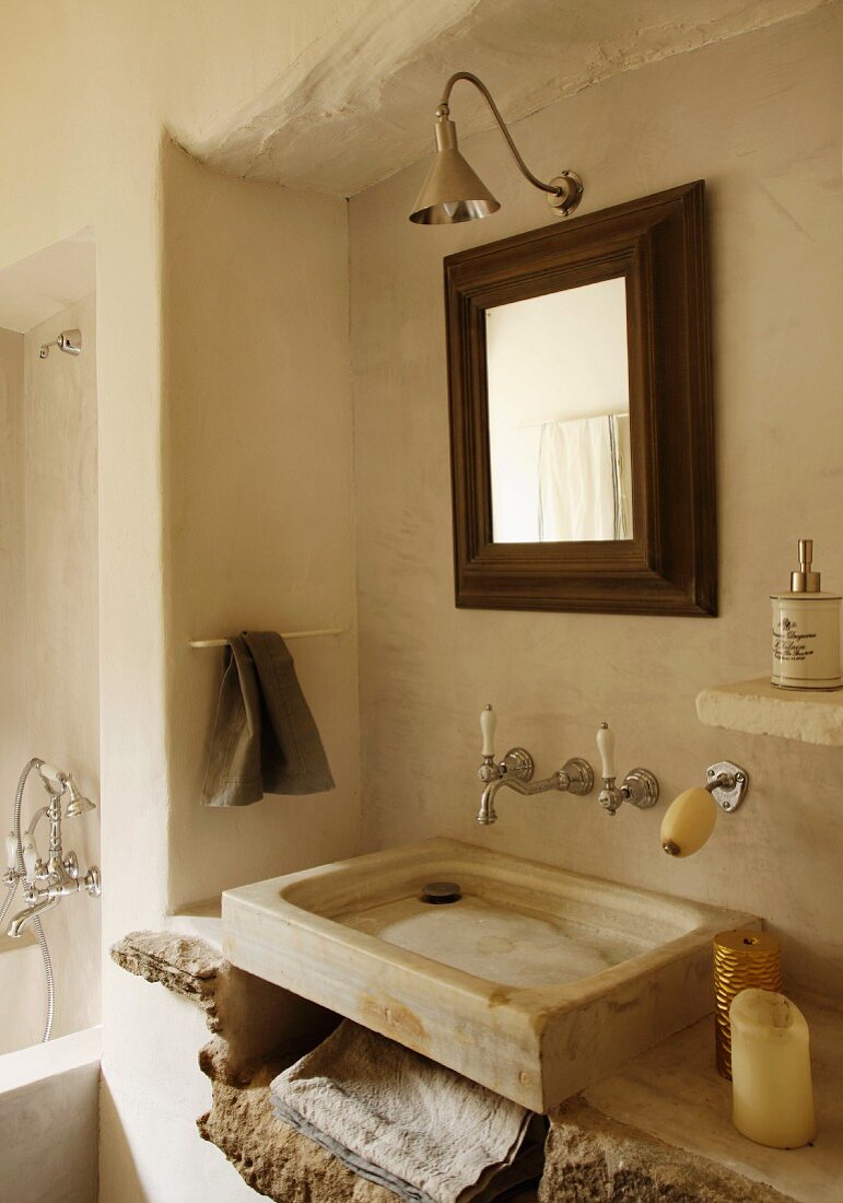Simple, stone, counter-top wash basin with vintage, wall-mounted tap fittings and framed mirror in rustic bathroom
