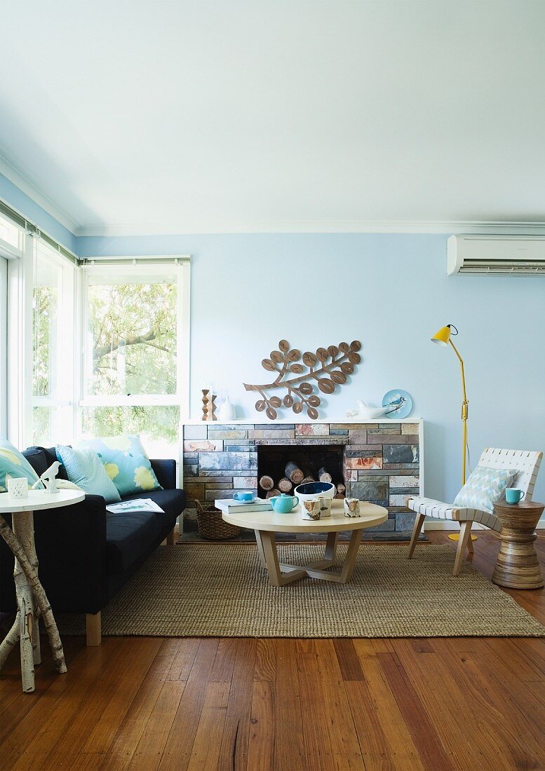 60's living room with wooden coffee table on a sisal rug and black couch in front of a fireplace in a bright blue room