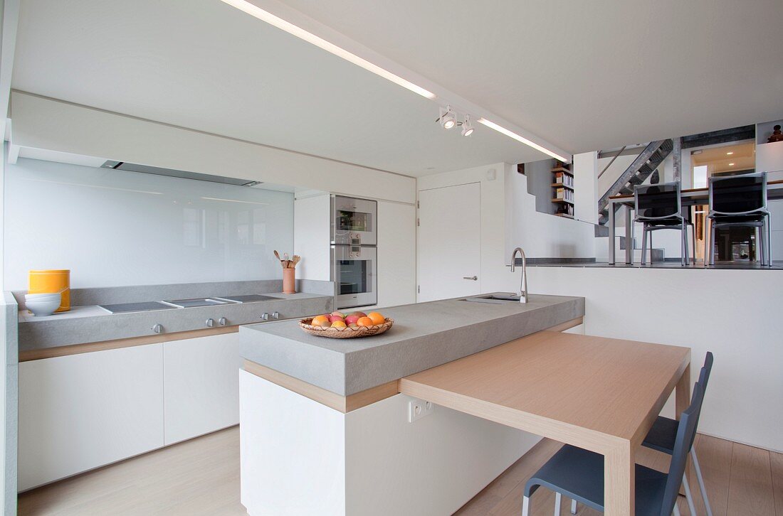 Blick von minimalistischer Küche mit Frühstückstheke auf den höhergelegenen Essplatz