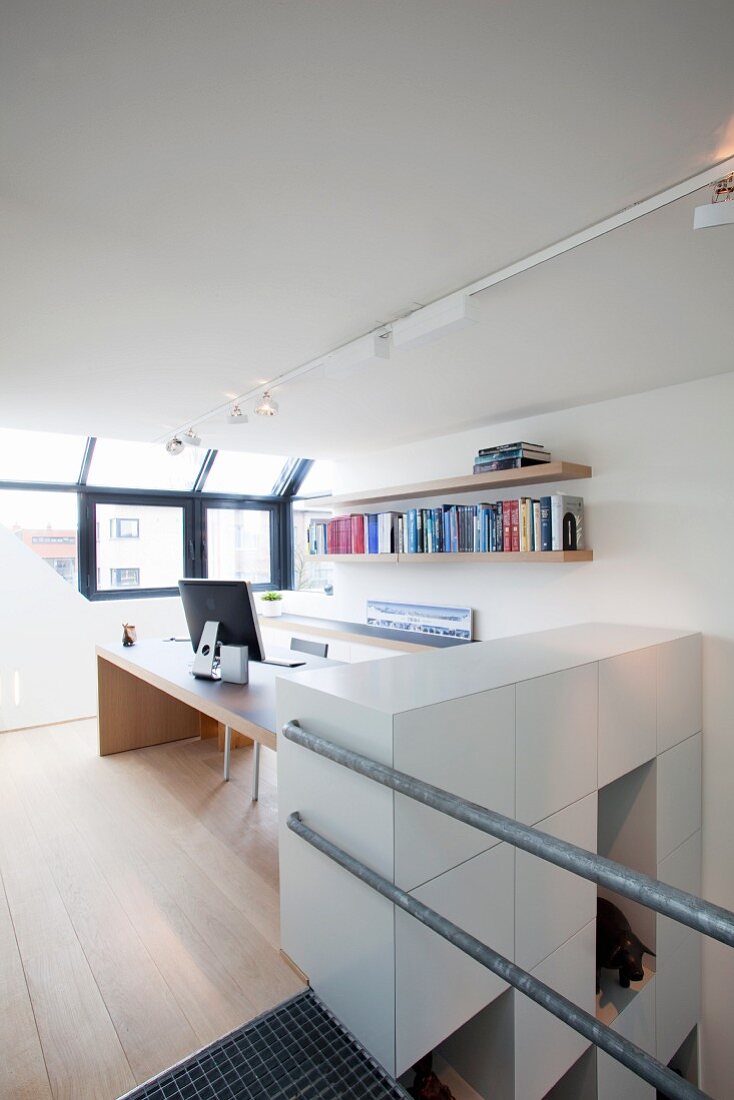 Hellse Arbeitszimmer mit Schreibtisch und Bücherbord; brüstungshohe Elementwand an der Treppe