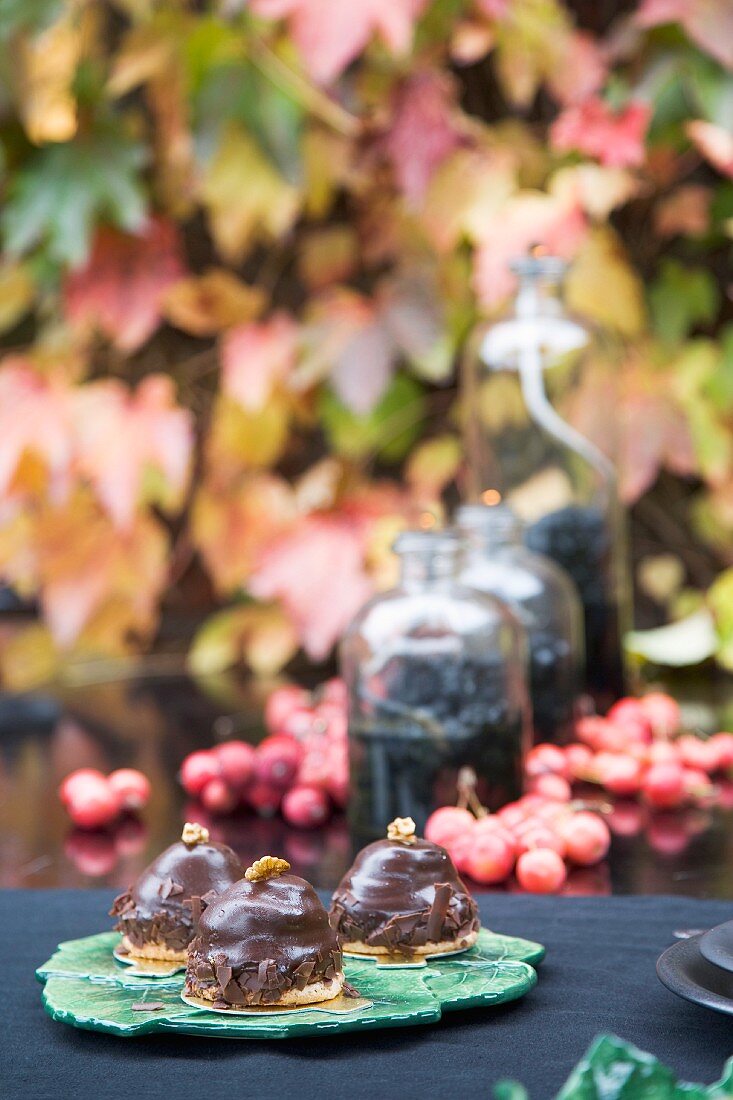 Chocolate pastries & autumnal arrangement of oil lamps & autumn fruits on garden table