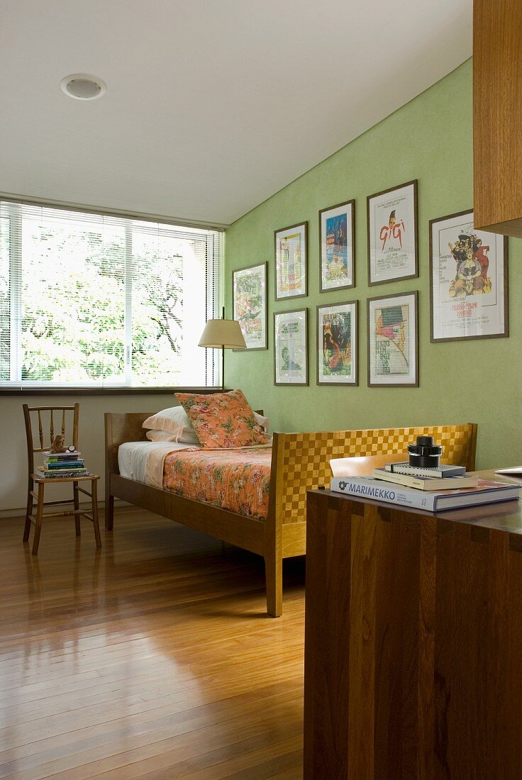 Schlafraum mit kunsthandwerklich gearbeitetem Bett vor gerahmten Plakaten auf lindgrün getönter Wand