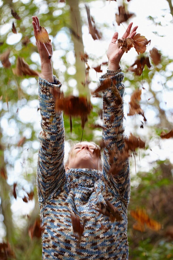 Frau wirft herbstliche Blätter in die Luft