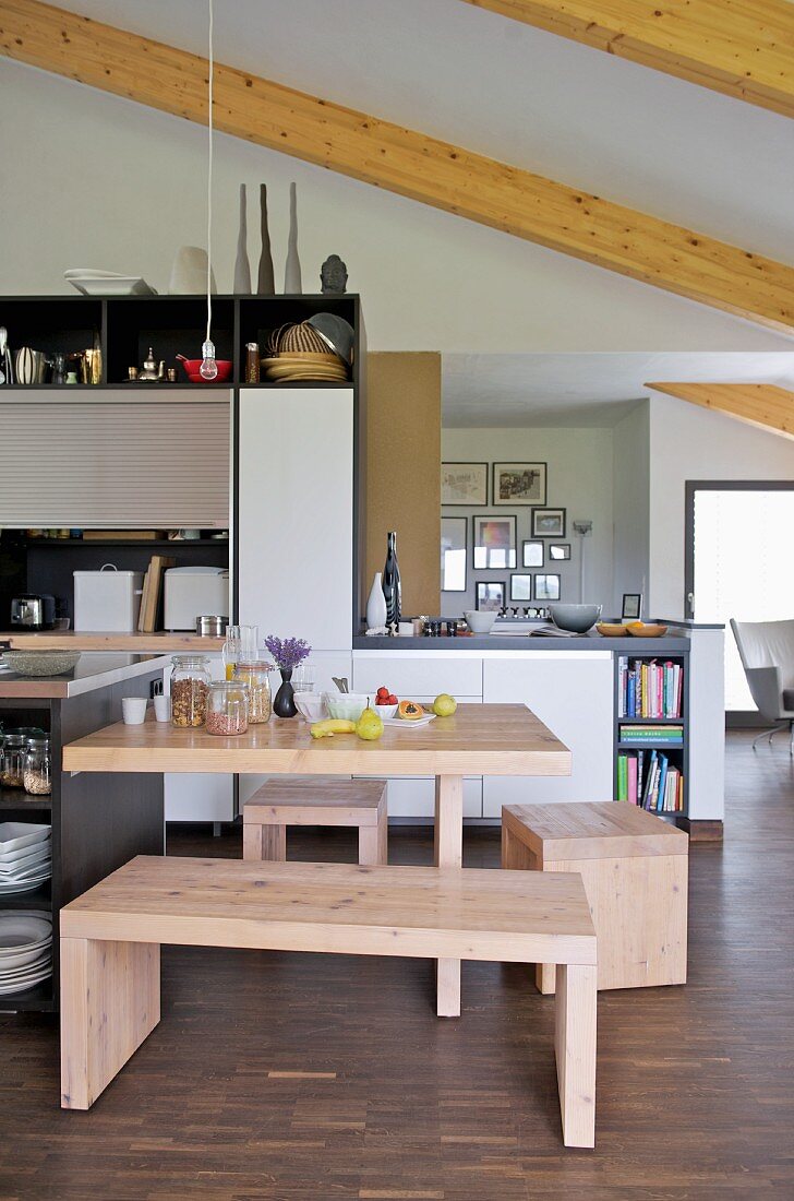 Helle Holzbank und Hocker um Esstisch in offener, moderner Küche mit Holzbalkendecke