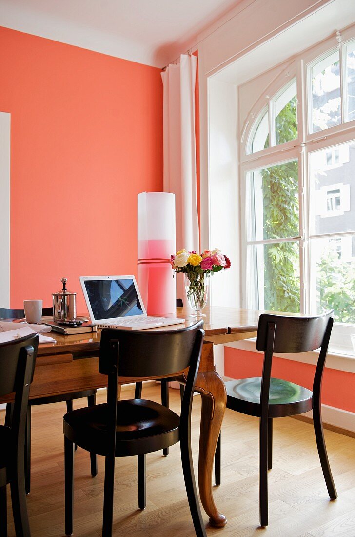 Work area on antique wooden table next to window in room with salmon pink wall