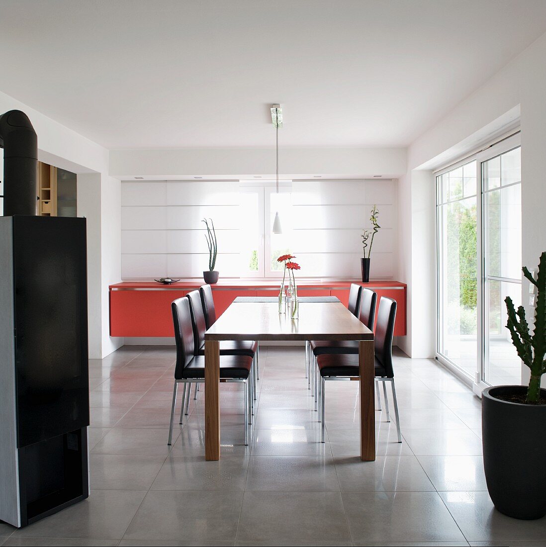 Modern dining table and leather-covered chairs in front of red sideboard against closed panel curtains on windows