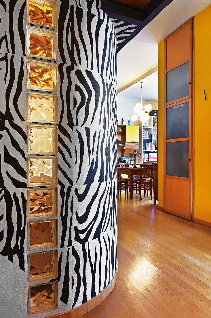 Foyer with zebra patterned curved wall and yellow-painted wall next to open-plan dining room
