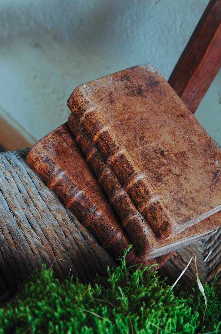 Abgegriffene, antiquarische Bücher mit Ledereinband auf der geflochtenen Sitzfläche eines alten Stuhls