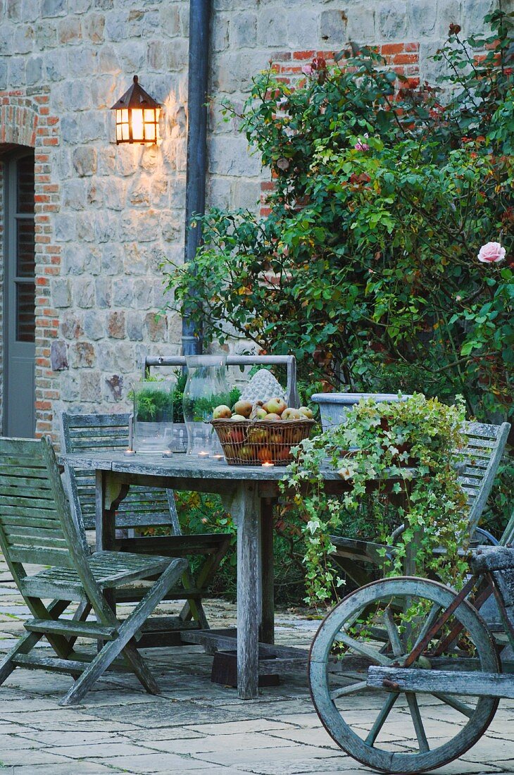 Terrace seating area with faded wooden furniture in front of climber-covered facade of old, French stone house