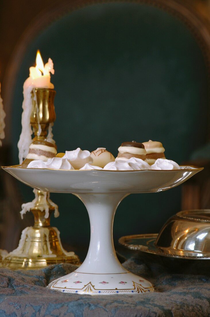 Pralinen Konfekt auf Porzellanschale mit Fuss vor Messing-Kerzenständer und brennender Kerze