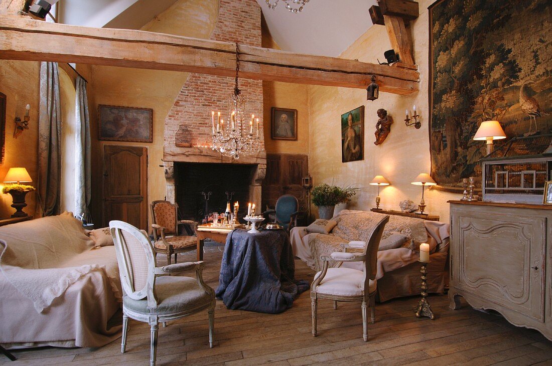 Sessel im Rokokostil und Sofa um Tisch mit drapiertem Tischtuch in rustikalem Wohnzimmer mit Holzkonstruktion