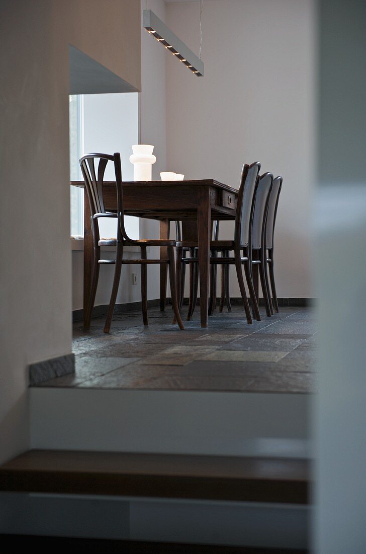 Simple dining table and chairs below pendant lamp next to window