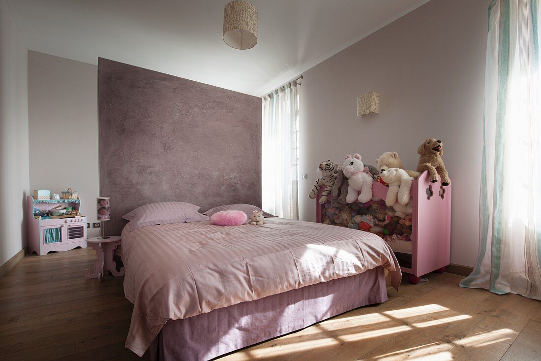 Doppelbett vor fliederfarbenem Raumteiler und halbhohes Regal mit Stofftieren in modernem Schlafzimmer