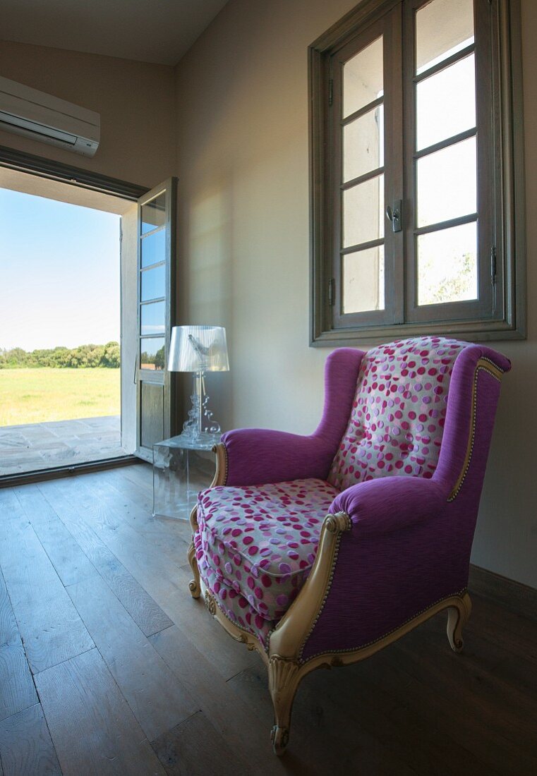 Rokoko-Lesesessel mit Designer Stoffbezug und farbigem Punktemuster in minimalistischem Raum mit traditionellem Flair und Blick durch offene Gartentür in die Landschaft
