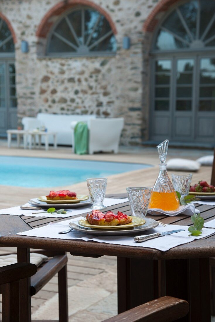Nachmittagskuchen auf Terrassentisch im Innenhof einer mediterranen Wohnanlage mit Pool