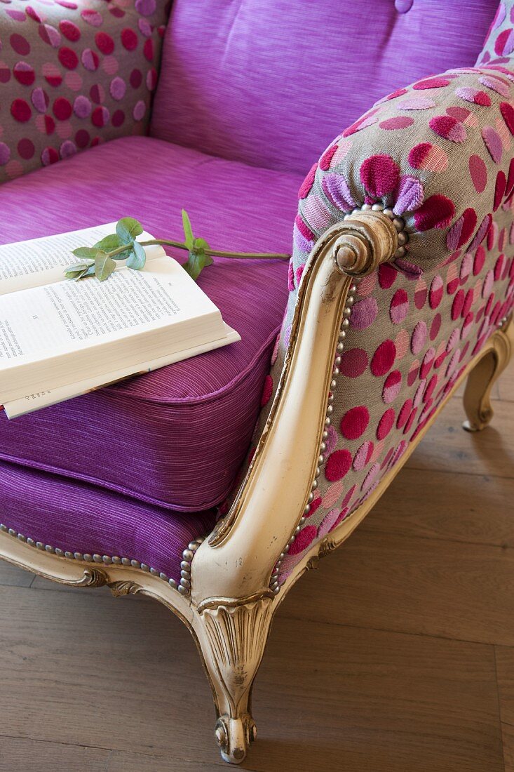 Book on reading chair with gilt wooden frame and colourful, spotted modern upholstery