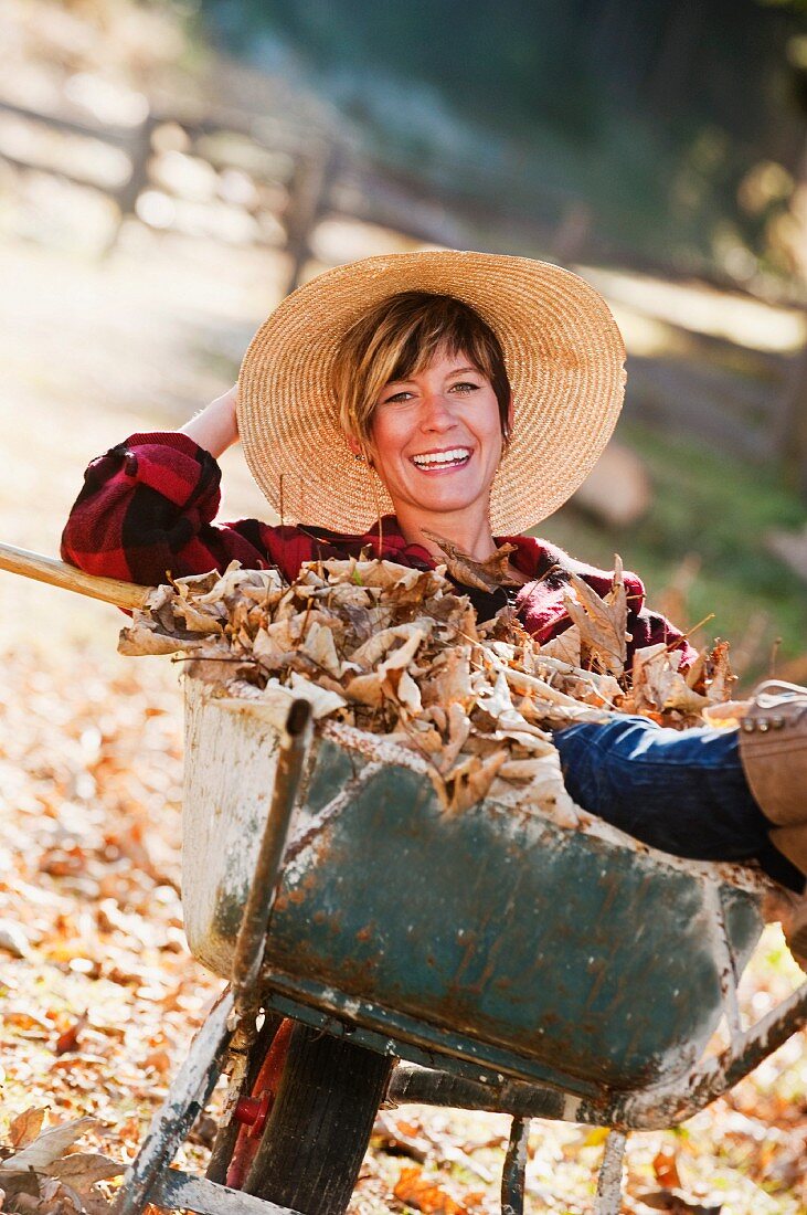 Frau sitzt in einer Schubkarre mit Herbstlaub im Garten