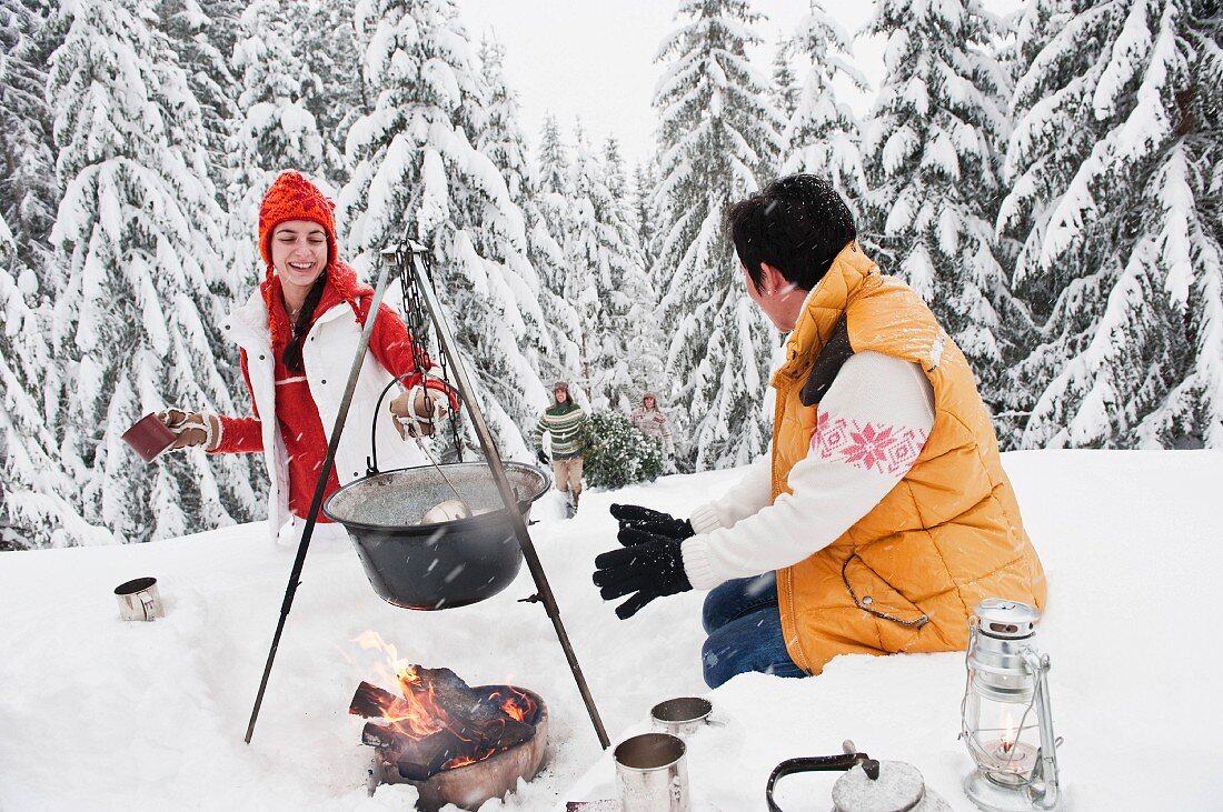 Paar kocht Weihnachtsessen am Lagerfeuer im verschneiten Wald