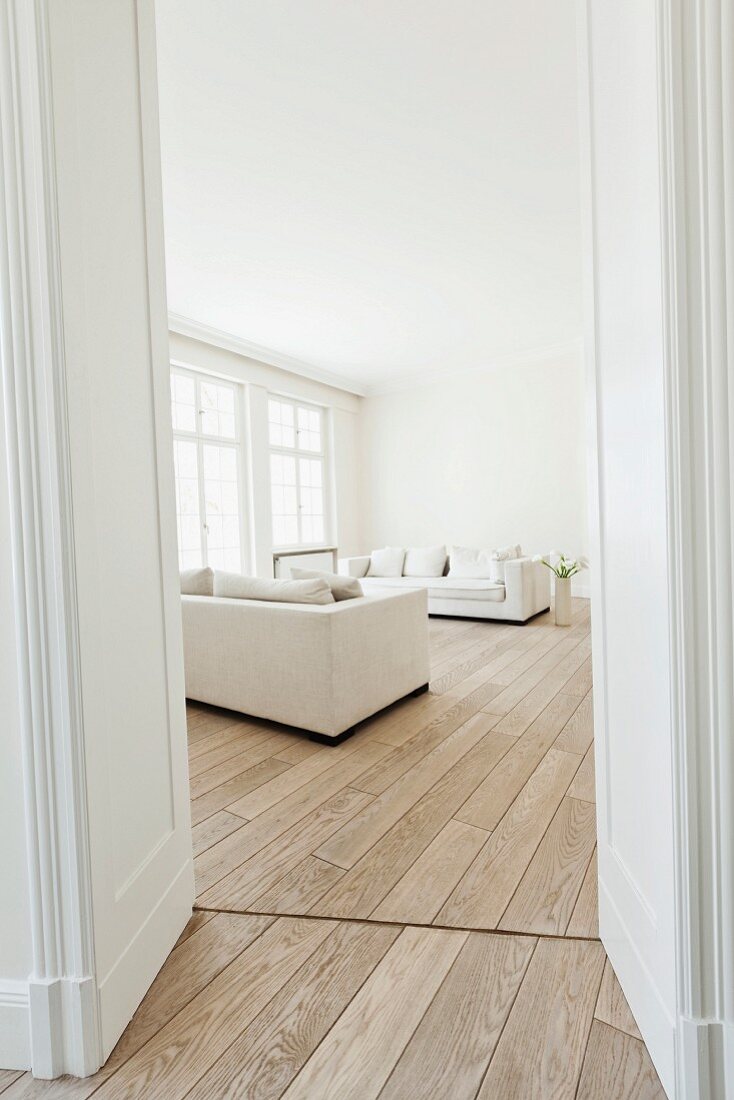 Bright, modern interior with white sofas, wooden floor, floor-to-ceiling windows and double doors