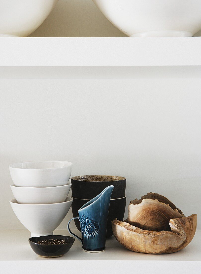 Various items of crockery made of china, ceramics and wood arranged on white shelf