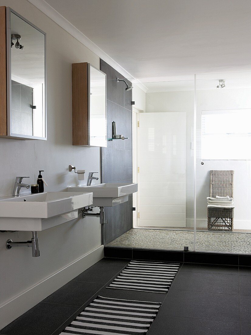 Two washbasins below mirrored cabinets and shower area with glass partition in modern bathroom