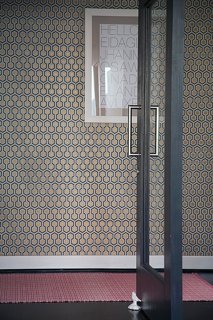 View through open glass door of framed calligraphy on patterned wallpaper