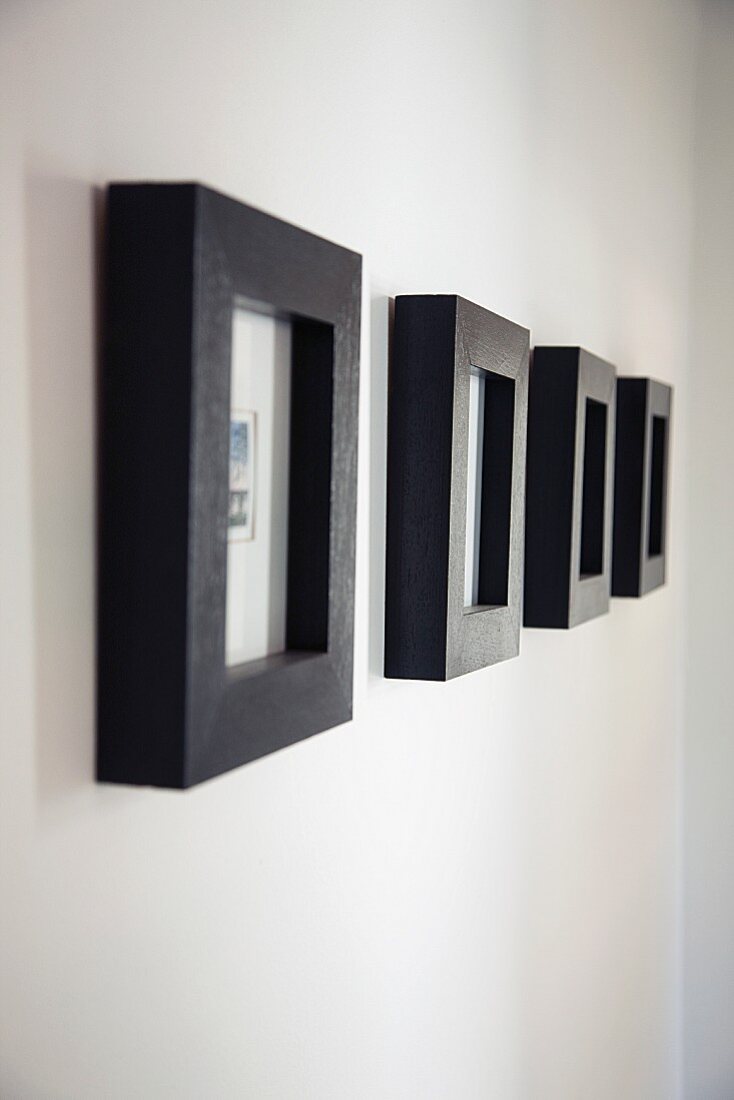 Eine Reihe kleiner Kunstbilder in breiten, schwarzen Rahmen an weißer Wand