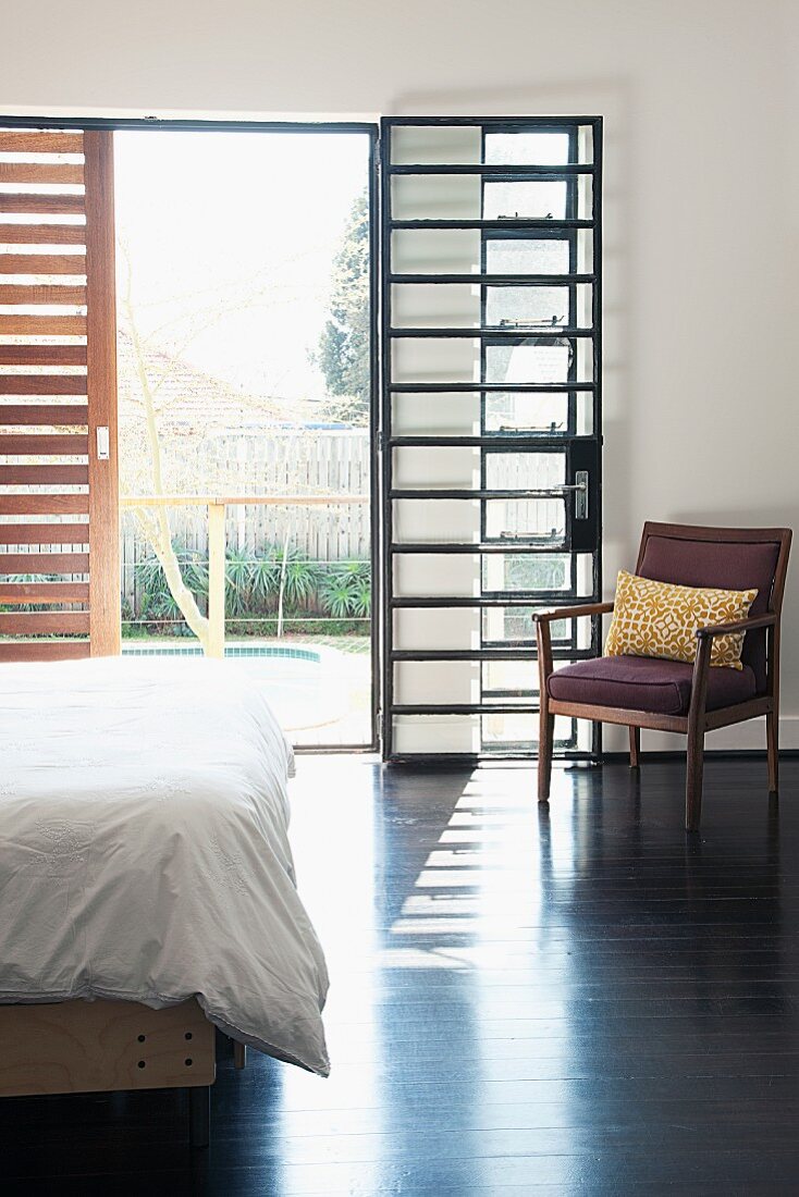 Retro Stuhl im sonnigen Schlafzimmer mit industrieverglaster Fenstertür und Holzschiebeladen