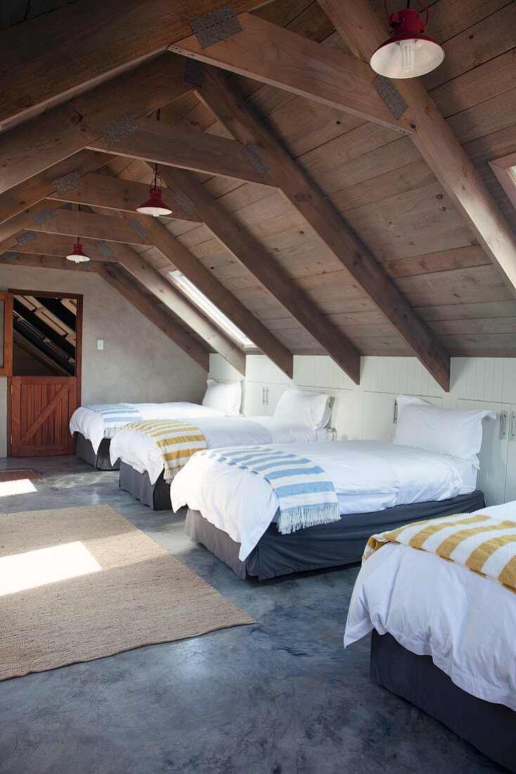 Several single beds with striped blankets in attic storey with exposed roof structure