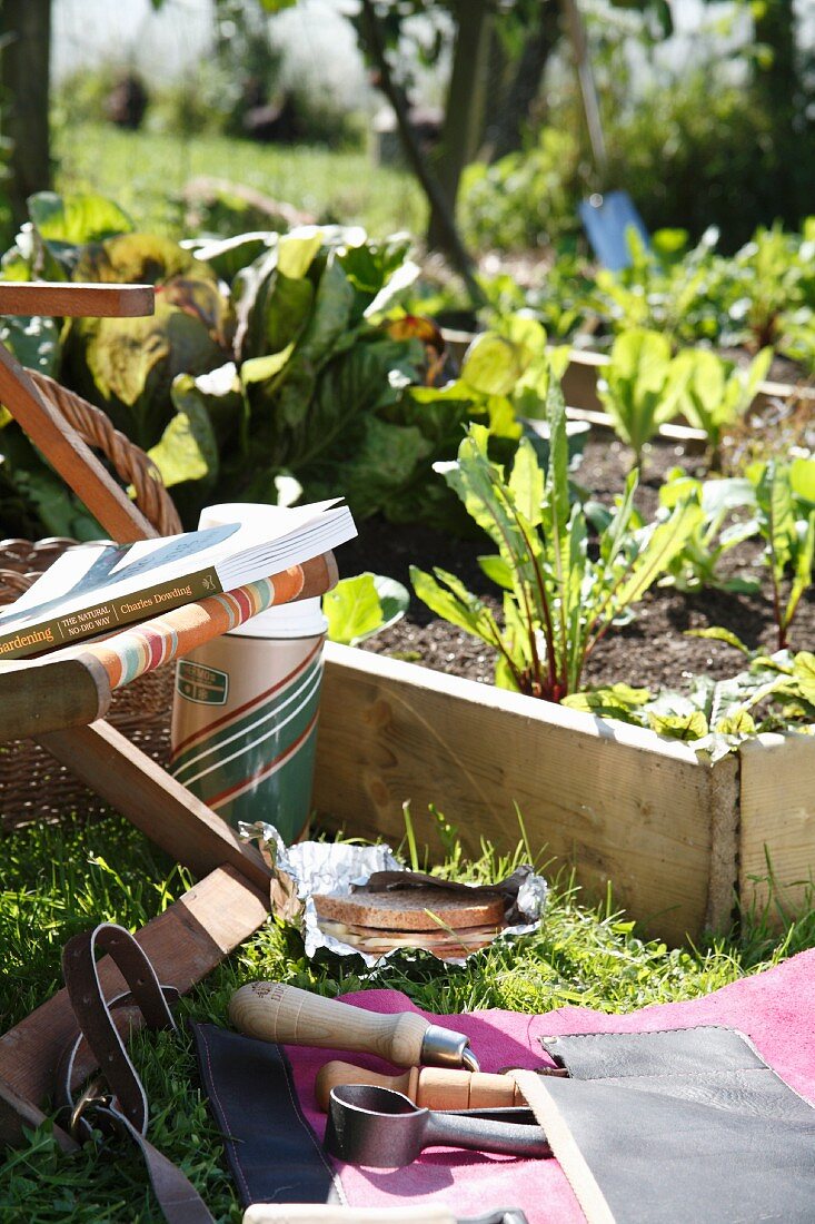 Garden tools and a garden chair next to a raised vegetable plot with a wooden surround