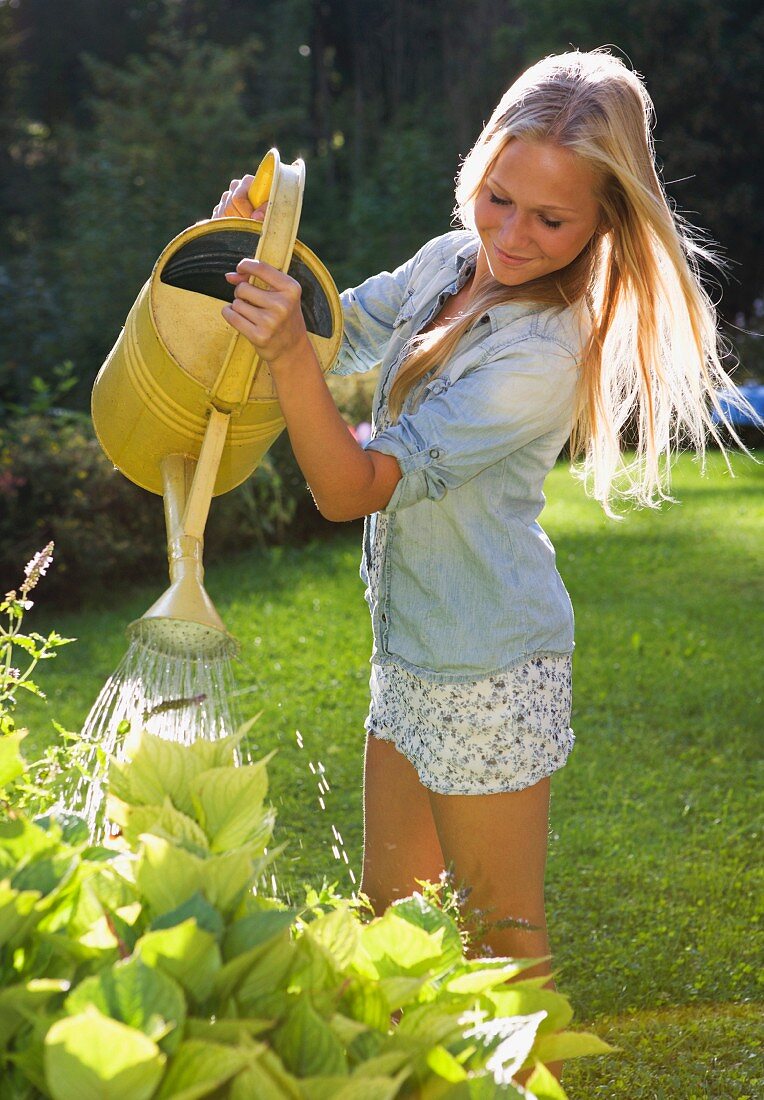 Blonder Teenager giesst die Pflanzen im Garten