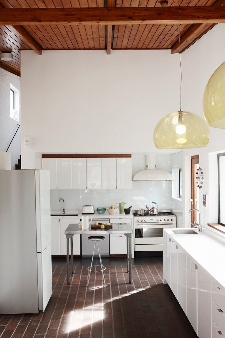 Pendant lamps with glass lampshades in white designer kitchen with dark terracotta floor